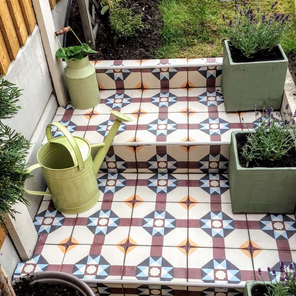 Garden steps featuring London Streets Berlin Street 20x20cm Victorian Moroccan style floor tiles, styled with potted plants and a watering can, showcasing a decorative patterned outdoor tile design in soft blue, burgundy and cream tones.
