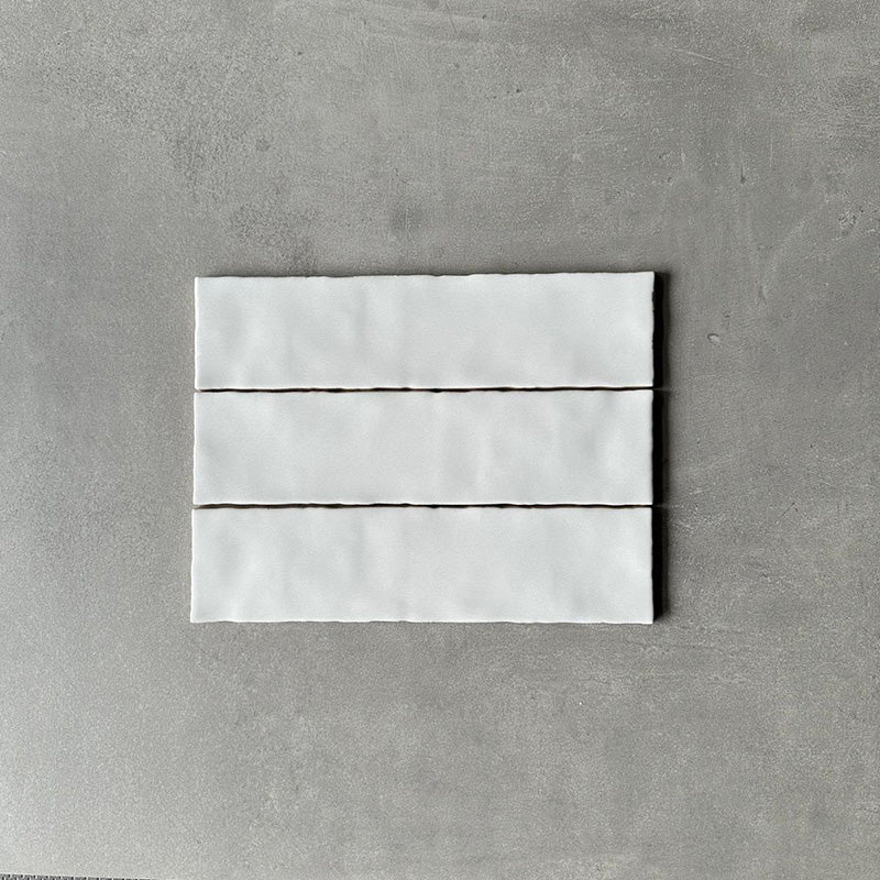 Three Nairobi gloss white handmade-effect tiles shown together, highlighting the subtle tonal variation, lightly textured glazed surface and gently uneven edges of the rustic finish.