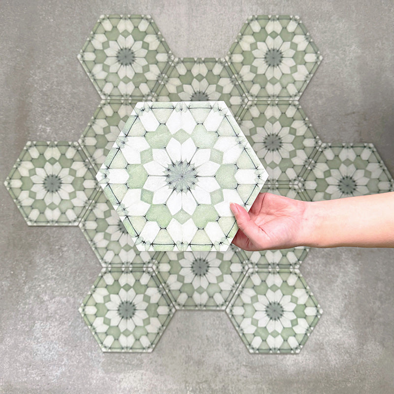 Hand holding Medina Soft Green Moroccan-style hexagon porcelain tile, 18.7 × 21.6 cm, shown against a grouped layout to highlight the repeating geometric pattern and soft green tones.