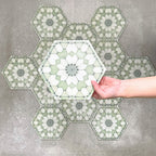 Hand holding Medina Soft Green Moroccan-style hexagon porcelain tile, 18.7 × 21.6 cm, shown against a grouped layout to highlight the repeating geometric pattern and soft green tones.