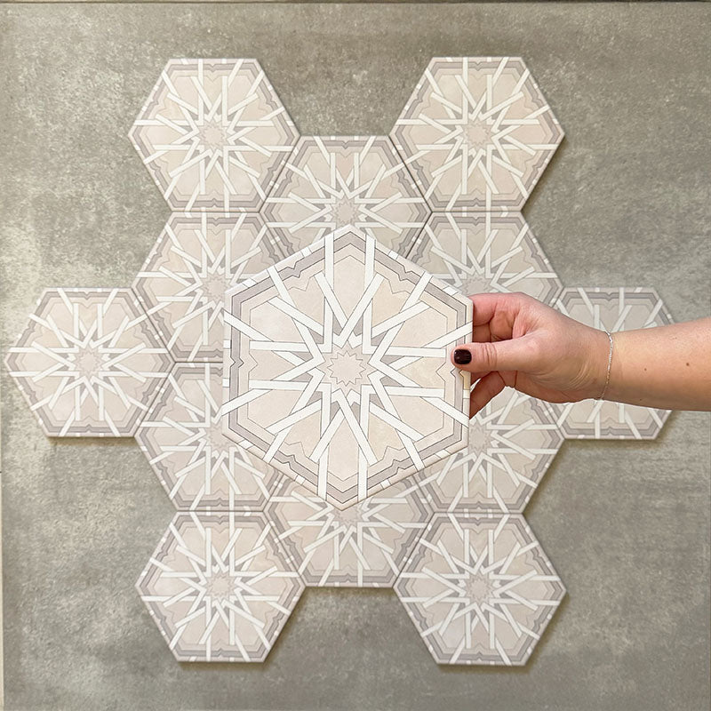 Hand holding Medina Hormuz Snow White Moroccan-style hexagon porcelain tile, 18.7 × 21.6 cm, shown against a grouped layout to highlight the crisp star-inspired geometric pattern in white and soft grey tones.