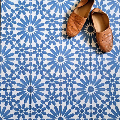 Fez Azure Blue 20x20cm Moroccan-style porcelain floor tiles arranged in a repeating geometric pattern, featuring crisp blue and white star motifs, styled with tan leather slippers for a relaxed, Mediterranean-inspired look.