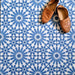 Fez Azure Blue 20x20cm Moroccan-style porcelain floor tiles arranged in a repeating geometric pattern, featuring crisp blue and white star motifs, styled with tan leather slippers for a relaxed, Mediterranean-inspired look.