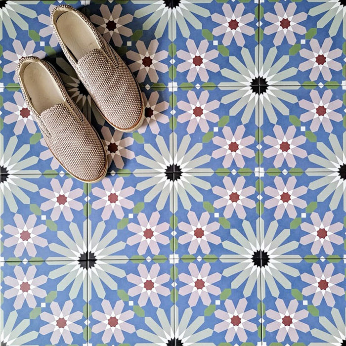 Fez Artisan 20x20cm Moroccan-style porcelain floor tiles arranged in a repeating geometric pattern, featuring soft blue, white, green and terracotta star motifs, styled with woven slip-on shoes for a relaxed, artisanal look.