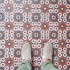 Fez Rosso Moroccan-style porcelain tiles laid in a neat grid, creating a rich, rhythmic pattern across the floor. Warm terracotta red starbursts sit against a soft grey-blue base, balanced by delicate blush pink and white geometric details inspired by traditional Moroccan tilework. Styled here with neutral footwear for scale, the design feels bold yet refined—perfect for adding warmth and character to kitchens, hallways or statement floor spaces while remaining practical and durable in porcelain.