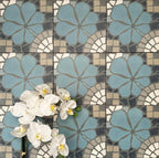 Nantes Azul Blue Moroccan-style patterned tiles laid in a repeating grid, shown in a 20x20cm format. The design features soft blue floral motifs combined with mosaic-effect detailing in muted greys, stone and white, creating a decorative, handcrafted look typical of traditional Moroccan floor tiles.