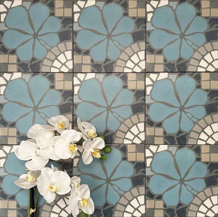 Nantes Azul Blue Moroccan-style patterned tiles laid in a repeating grid, shown in a 20x20cm format. The design features soft blue floral motifs combined with mosaic-effect detailing in muted greys, stone and white, creating a decorative, handcrafted look typical of traditional Moroccan floor tiles.