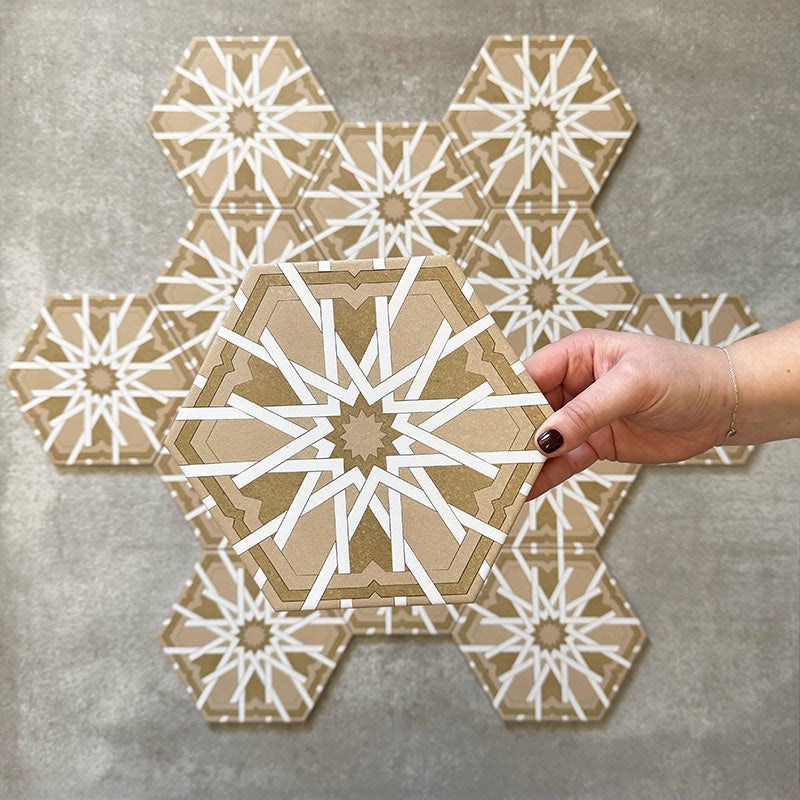Hand holding Medina Hormuz Vintage Gold Moroccan-style hexagon porcelain tile, 18.7 × 21.6 cm, shown against a grouped layout to highlight the bold star-inspired geometric pattern in warm gold and white tones.