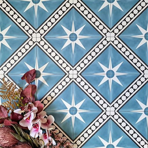 Gilgamesh Blue Moroccan style 20x20cm patterned tiles, shown in a flat lay with decorative foliage highlighting the blue, black and white geometric star design.