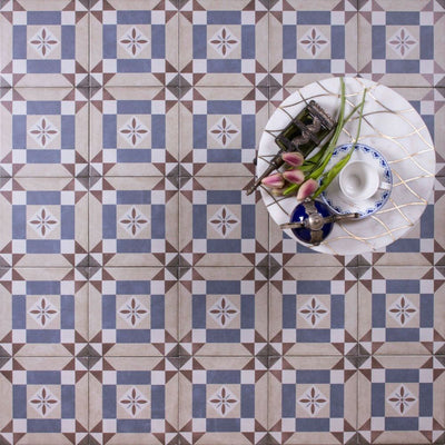 Viscount Harley Street 20×20cm Victorian-style porcelain wall and floor tiles laid in a repeating geometric square pattern in soft blue, beige and warm grey tones, shown as a full tile layout styled with a small table, decorative accessories and floral accents.
