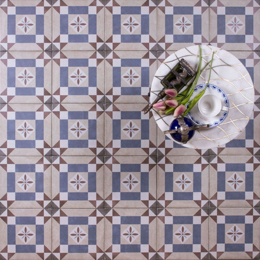 Viscount Harley Street 20×20cm Victorian-style porcelain wall and floor tiles laid in a repeating geometric square pattern in soft blue, beige and warm grey tones, shown as a full tile layout styled with a small table, decorative accessories and floral accents.