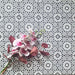 Fez Mini Winter Moroccan-style porcelain tiles laid in a repeating pattern, featuring a crisp black and white geometric star design. The 15 × 15cm encaustic-effect tiles create a bold yet timeless look, with intricate detailing that adds depth and rhythm across the surface. Styled with soft pink florals for contrast, this design is ideal for statement floors, splashbacks, or feature walls in both modern and classic interiors.
