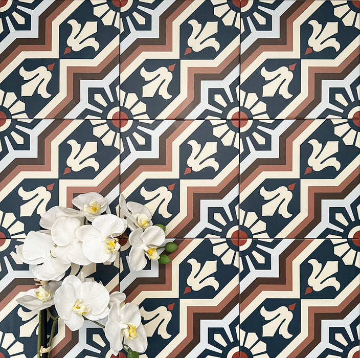 Close-up of Balthazar Grand 20×20cm Moroccan-style porcelain tiles laid in a repeating pattern, highlighting the bold geometric design in deep blue, warm brown and soft cream tones, styled with white orchid flowers to showcase the intricate encaustic-inspired detail and matt finish.