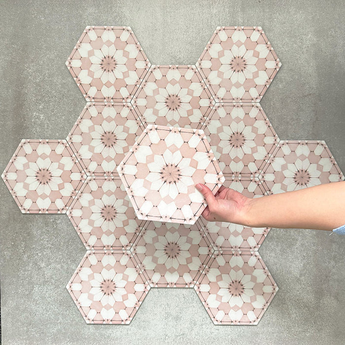Hand holding Medina Dusty Pink Moroccan-style hexagon porcelain tile, 18.7 × 21.6 cm, shown against a grouped layout to highlight the repeating geometric pattern in soft pink and white tones.