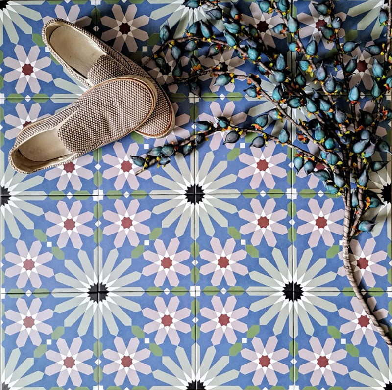 Fez Artisan 20x20cm Moroccan-style porcelain floor tiles arranged in a repeating geometric pattern, featuring soft blue, white, green and terracotta star motifs, styled with woven slip-on shoes for a relaxed, artisanal look.