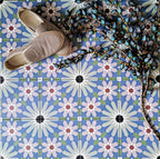 Fez Artisan 20x20cm Moroccan-style porcelain floor tiles arranged in a repeating geometric pattern, featuring soft blue, white, green and terracotta star motifs, styled with woven slip-on shoes for a relaxed, artisanal look.