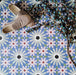 Fez Artisan 20x20cm Moroccan-style porcelain floor tiles arranged in a repeating geometric pattern, featuring soft blue, white, green and terracotta star motifs, styled with woven slip-on shoes for a relaxed, artisanal look.