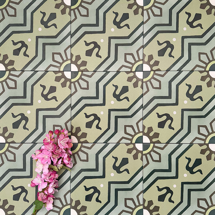 Close-up of Balthazar Verde 20×20cm Moroccan-style porcelain tiles laid in a repeating pattern, highlighting the encaustic-inspired geometric design in layered green tones with dark accents, styled with pink flowers to emphasise the intricate detailing and matt finish.
