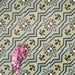 Close-up of Balthazar Verde 20×20cm Moroccan-style porcelain tiles laid in a repeating pattern, highlighting the encaustic-inspired geometric design in layered green tones with dark accents, styled with pink flowers to emphasise the intricate detailing and matt finish.