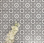 Fez Mini Winter Moroccan-style porcelain tiles shown laid in a repeating pattern, featuring a striking black and white geometric star design inspired by traditional Moroccan motifs. The 15 × 15cm tiles create a bold, high-contrast surface with intricate detailing, styled here with white flowers for a clean, elegant look—ideal for statement floors, splashbacks, or feature walls in both modern and classic interiors.