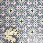 Fez Artisan 20x20cm Moroccan-style porcelain wall tiles arranged in a repeating geometric pattern, featuring soft blue, blush pink, green and terracotta star motifs, styled with white orchid flowers for a warm, decorative finish.