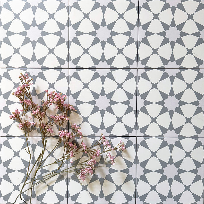 Agadir Silver Moroccan-style 20x20cm porcelain tiles arranged in a repeating geometric pattern, shown as a group layout with soft grey detailing and delicate pink flowers for a calm, contemporary look.