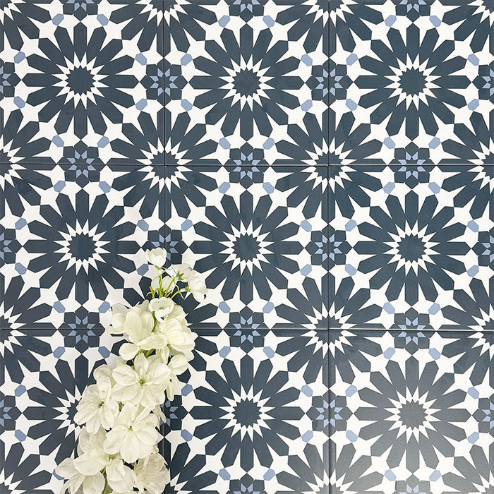 Fez Federal Blue 20x20cm Moroccan-style porcelain wall tiles arranged in a repeating geometric pattern, featuring bold navy blue and white star motifs with subtle pale blue detailing, styled with white floral accents for a crisp, decorative finish.