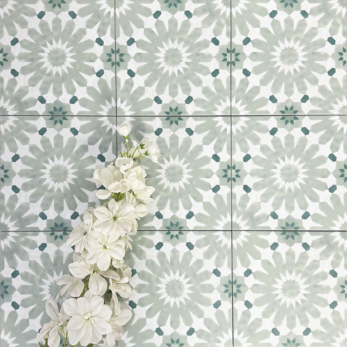 Fez Jade Green 20x20cm Moroccan-style porcelain wall tiles arranged in a repeating geometric pattern, featuring soft jade green and white star motifs, styled with trailing white flowers for a calm, decorative finish.