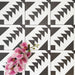 Almeira Azteca Moroccan-style porcelain tiles arranged in a repeating pattern, highlighting the bold black and white geometric design with stepped triangles, styled with pink flowers for contrast, 20x20cm.