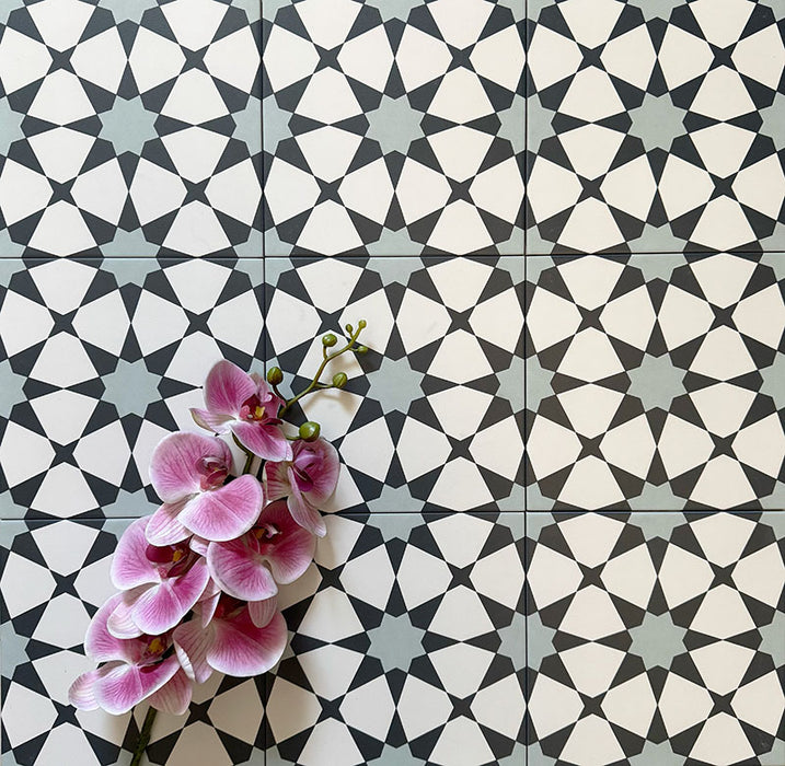 Agadir Azul Blue Moroccan-style 20x20cm porcelain floor tiles laid in a repeating geometric star pattern in blue, black and white, styled with a decorative orchid to highlight the intricate design.