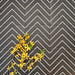 Grouped Almeria Jilani Black Moroccan-style porcelain wall and floor tiles arranged in a repeating white line chevron pattern, 20x20cm, styled with yellow florals to highlight the geometric design.