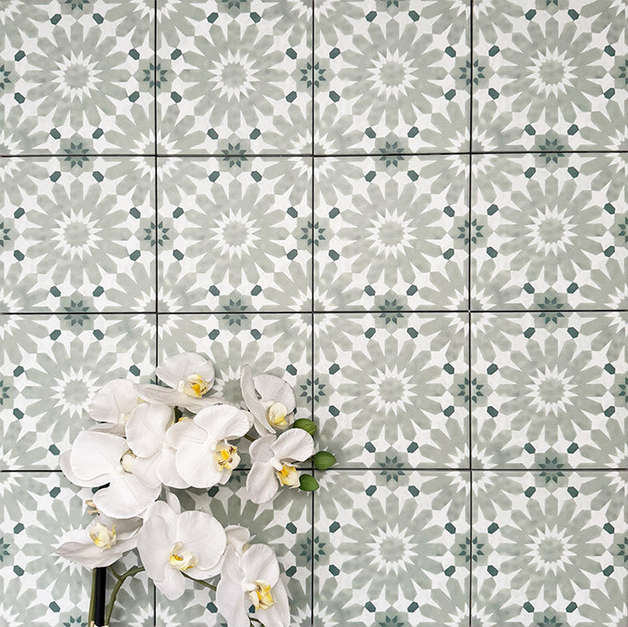 Fez Mini Jade Green 15x15cm Moroccan-style porcelain wall tiles arranged in a repeating geometric pattern, featuring soft jade green and white star motifs, styled with white orchid flowers for a fresh, elegant finish.