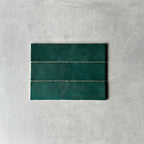 Three Nairobi gloss moss green handmade-effect tiles shown together, highlighting natural tonal variation, lightly textured glazing and the gently uneven edges of the rustic finish.