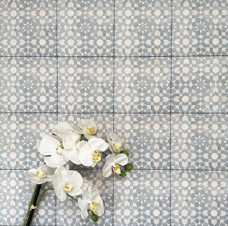 Berber Tetuan Blue 15×15cm Moroccan-style porcelain tiles laid in a grid pattern, showcasing a soft blue and cream geometric design with decorative floral styling.