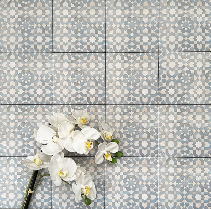 Berber Tetuan Blue 15×15cm Moroccan-style porcelain tiles laid in a grid pattern, showcasing a soft blue and cream geometric design with decorative floral styling.