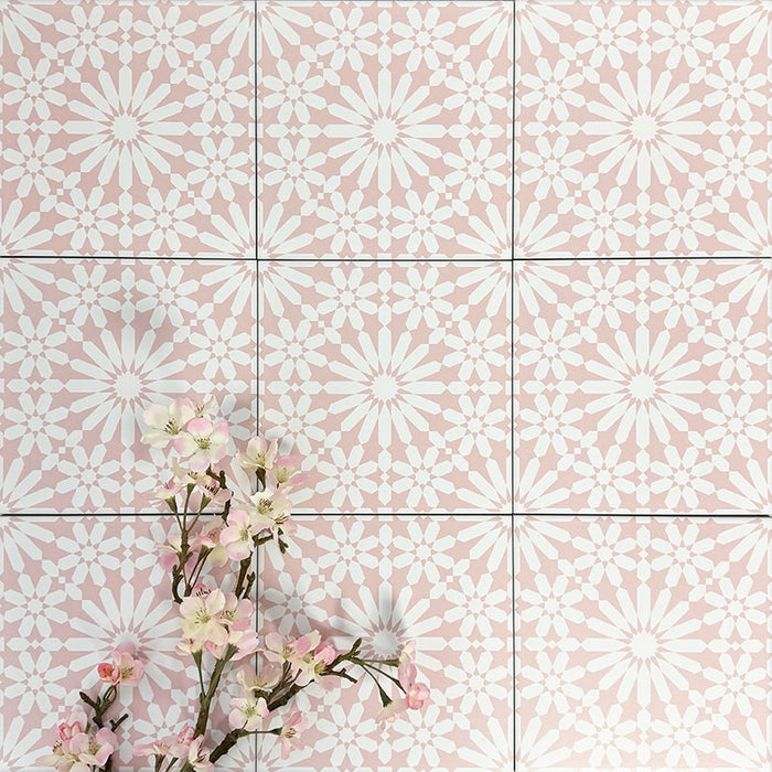 Fez Rose Pink Moroccan-style porcelain tiles laid in a repeating grid, creating a soft, decorative pattern across the surface. The blush pink background is paired with a crisp white geometric starburst motif, forming a delicate yet eye-catching design inspired by traditional Moroccan tiles. Styled with pale pink blossom branches in the corner, the overall look feels light, elegant and feminine—perfect for adding subtle pattern and warmth to bathrooms, kitchens or feature walls.