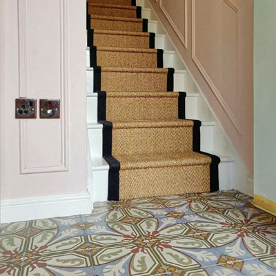 Victorian-style hallway featuring Viscount Langholme Place 20×20cm porcelain wall and floor tiles laid in a repeating floral and geometric pattern in soft blue, sage green, warm red and cream tones, styled alongside a classic staircase with natural sisal runner, white panelling and traditional detailing.