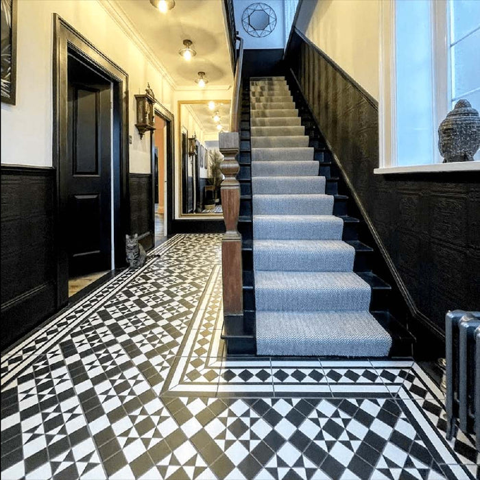 Hallway featuring Dorset Tile Black & White Victorian-style porcelain floor tiles in a 25 × 25cm format, laid in a striking geometric pattern with a decorative border, paired with a classic staircase, black wood panelling and traditional period details.