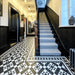 Hallway featuring Dorset Tile Black & White Victorian-style porcelain floor tiles in a 25 × 25cm format, laid in a striking geometric pattern with a decorative border, paired with a classic staircase, black wood panelling and traditional period details.