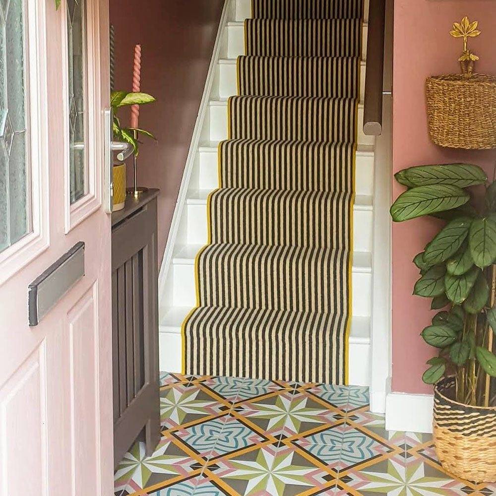 Entrance hallway featuring Cuba Star Moroccan-style porcelain floor tiles in a 20×20cm square format, laid in a repeating geometric star pattern with soft green, blue, pink and mustard tones, paired with blush pink walls and a striped stair runner for a bold yet welcoming interior.