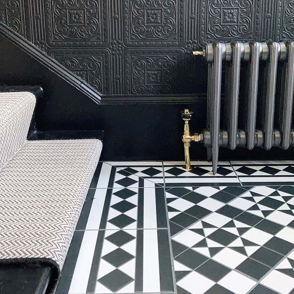 Hallway featuring Dorset Tile Black & White Victorian-style porcelain floor tiles in a 25 × 25cm format, laid in a striking geometric pattern with a decorative border, paired with a classic staircase, black wood panelling and traditional period details.