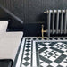Hallway featuring Dorset Tile Black & White Victorian-style porcelain floor tiles in a 25 × 25cm format, laid in a striking geometric pattern with a decorative border, paired with a classic staircase, black wood panelling and traditional period details.