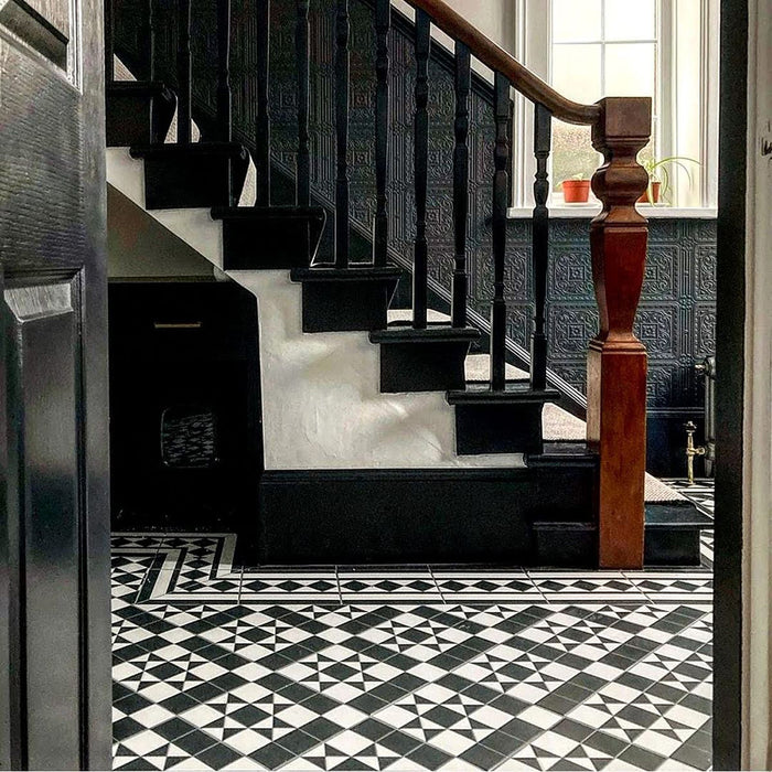 Hallway featuring Dorset Tile Black & White Victorian-style porcelain floor tiles in a 25 × 25cm format, laid in a striking geometric pattern with a decorative border, paired with a classic staircase, black wood panelling and traditional period details.