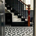 Hallway featuring Dorset Tile Black & White Victorian-style porcelain floor tiles in a 25 × 25cm format, laid in a striking geometric pattern with a decorative border, paired with a classic staircase, black wood panelling and traditional period details.