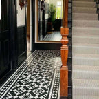 Hallway featuring Dorset Tile Black & White Victorian-style porcelain floor tiles in a 25 × 25cm format, laid in a striking geometric pattern with a decorative border, paired with a classic staircase, black wood panelling and traditional period details.
