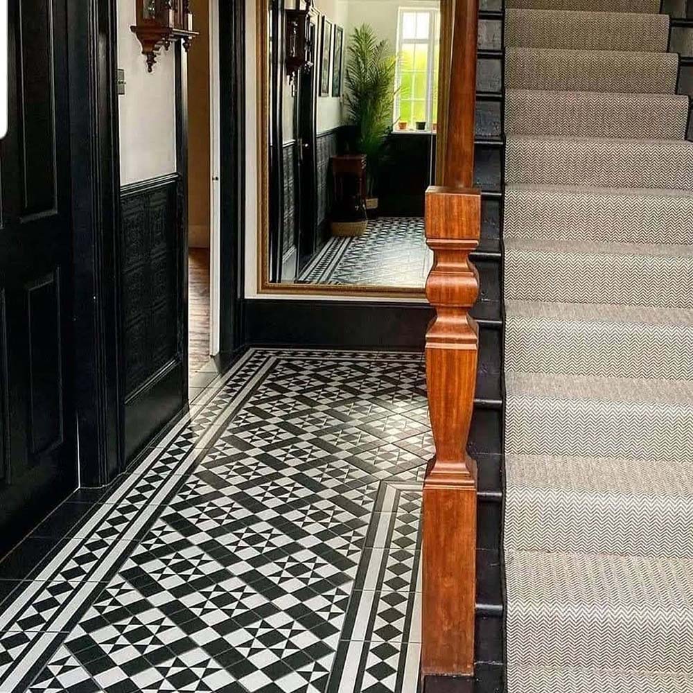 Hallway featuring Dorset Tile Black & White Victorian-style porcelain floor tiles in a 25 × 25cm format, laid in a striking geometric pattern with a decorative border, paired with a classic staircase, black wood panelling and traditional period details.