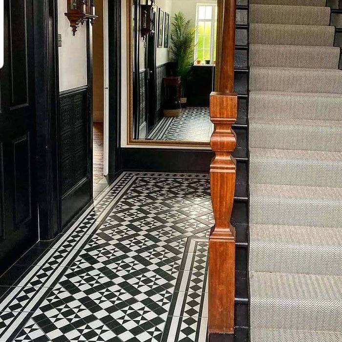 Hallway featuring Dorset Tile Black & White Victorian-style porcelain floor tiles in a 25 × 25cm format, laid in a striking geometric pattern with a decorative border, paired with a classic staircase, black wood panelling and traditional period details.