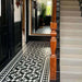 Hallway featuring Dorset Tile Black & White Victorian-style porcelain floor tiles in a 25 × 25cm format, laid in a striking geometric pattern with a decorative border, paired with a classic staircase, black wood panelling and traditional period details.