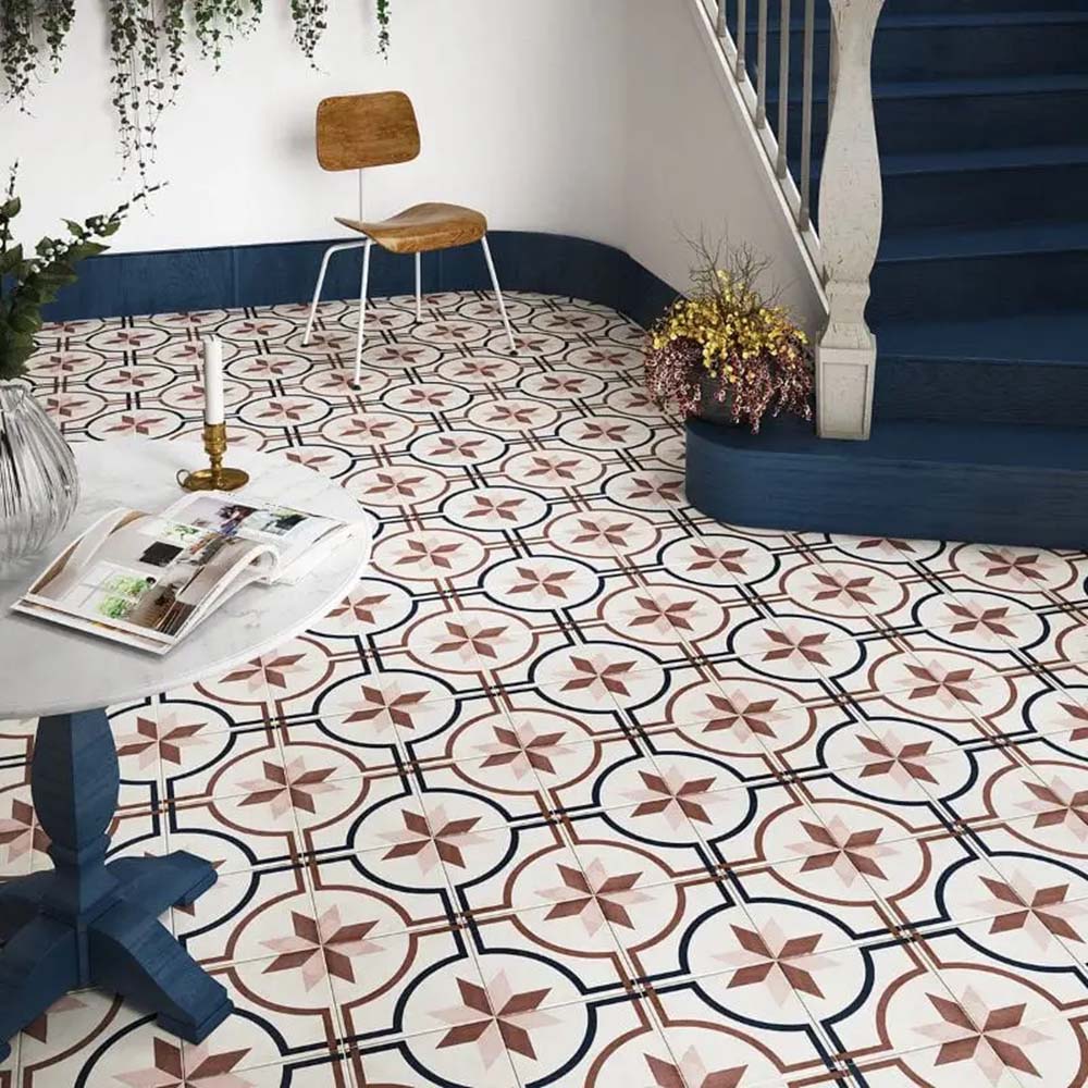 Victorian-style hallway featuring Viscount Rose 20×20cm porcelain wall and floor tiles laid in a classic geometric star and circular pattern in soft rose, navy and white, styled with a curved staircase, deep blue panelling, wooden accent furniture and decorative greenery for a timeless, elegant look.