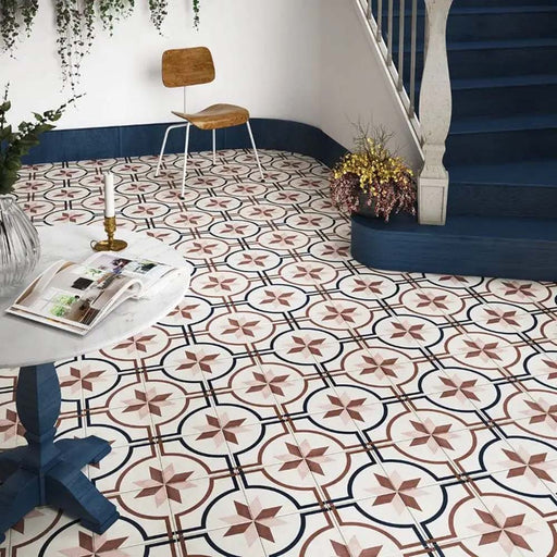 Victorian-style hallway featuring Viscount Rose 20×20cm porcelain wall and floor tiles laid in a classic geometric star and circular pattern in soft rose, navy and white, styled with a curved staircase, deep blue panelling, wooden accent furniture and decorative greenery for a timeless, elegant look.